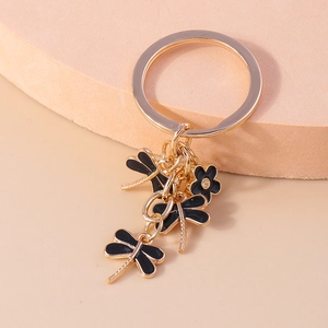 Detail of gold metal keychain featuring three black enamel dragonflies and a small flower
