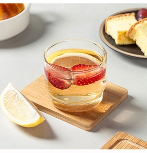 Close-up of clear stackable glass cup with lemon and strawberry on bamboo coaster