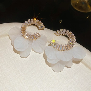 Macro shot of gold C-shaped earrings with zircon accents and white petal fringe details