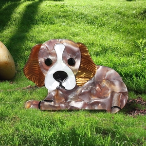 Close-up of a brown mottled acrylic dog brooch on green grass in natural light