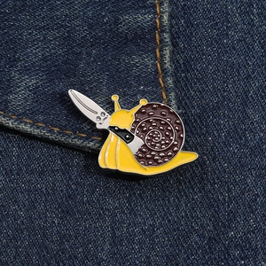 Detail of yellow enamel snail brooch with a knife on a dark denim fabric edge