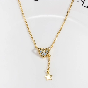 Detail of gold heart pendant with blue gem and star charm on white ceramic plate