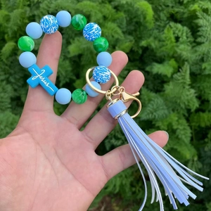 Beaded keychain bracelet with blue marble beads, Jesus cross, and tassel in outdoor view