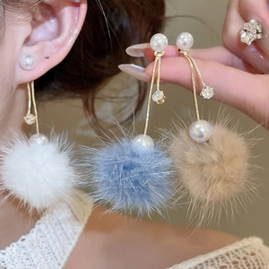 Detail of long pearl earrings with gold chains and colorful faux fur pom-poms on model
