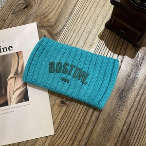 Gros plan d'un bandeau en tricot bleu sarcelle avec broderie Boston sur bois