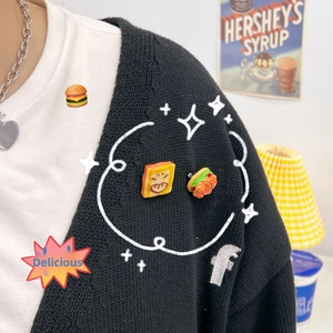 Detailed view of cute resin toast and burger pins worn on a black knit cardigan