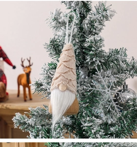 Close-up of a plush Christmas gnome ornament hanging on a snowy tree with festive decor