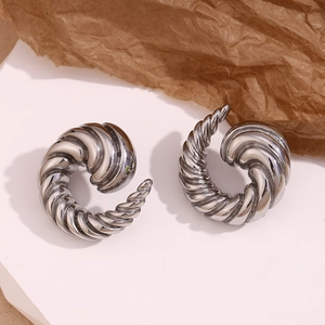 Detailed close-up of silver-tone spiral horn earrings on a minimalist white stand