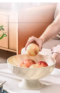 Close-up of placing an apple into a textured food-grade ivory white fruit bowl