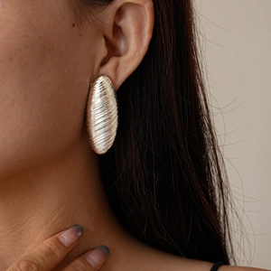 Close-up of silver brushed oval geometric stud earrings with vertical striped texture
