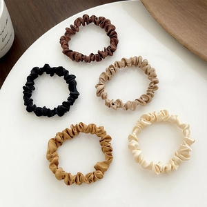 Detailed set of five assorted silk satin scrunchies displayed on a white ceramic plate