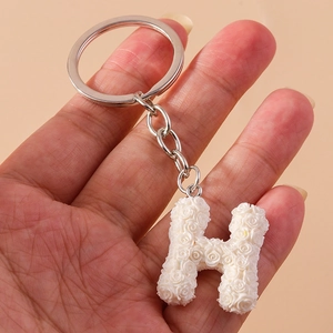 Macro shot of letter H keychain with white rose floral relief and silver metal chain