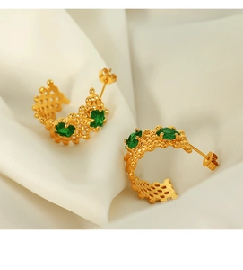 Gros plan sur des boucles d'oreilles en C plaquées or 18K et zircon vert sur soie blanche