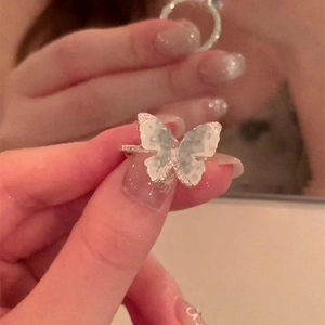 Handheld silver butterfly ring with iridescent gradient resin stone against a mirror background