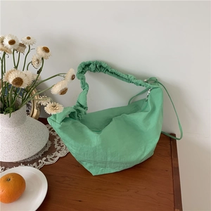 Borsa hobo in nylon verde chiaro con manico a pieghe su un tavolo in legno naturale
