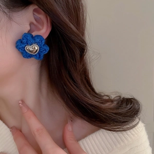 Close-up of a blue knitted flower earring with a silver heart center worn by a model