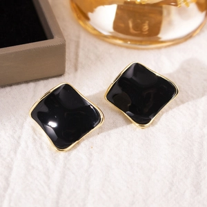 Close-up of square black enamel stud earrings with gold plating on white linen