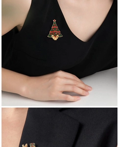 Close-up of a green enamel Christmas tree brooch with a golden bow on a black blazer lapel