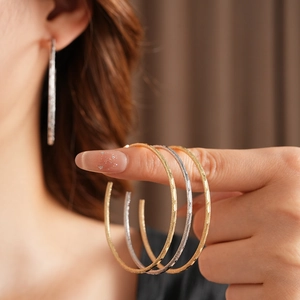 Dettaglio di orecchini tondi in oro e argento con texture opaca indossati e su mano