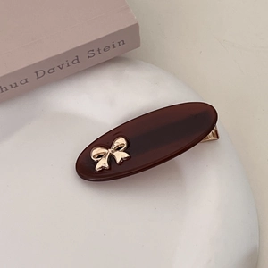 Detail shot of a dark brown oval hair clip with golden bow on a white ceramic plate