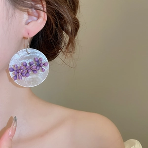 Detailed close-up of asymmetrical purple flower tassel earrings worn by a model