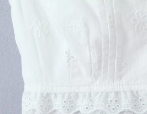 Détail de la broderie florale blanche et des bordures en dentelle sur haut en coton