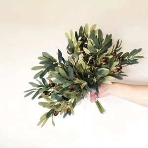 Artificial olive branches with green leaves and dark purple berries held in hand