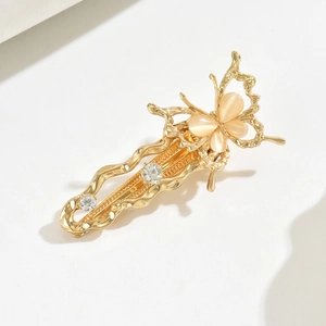 Close-up of golden metal butterfly hair clip with pink cat eye stone and clear rhinestones
