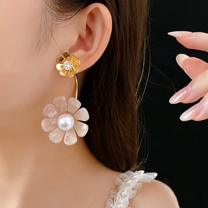 Detail view of a floral gold earring with pink shell luster and pearl center on a model