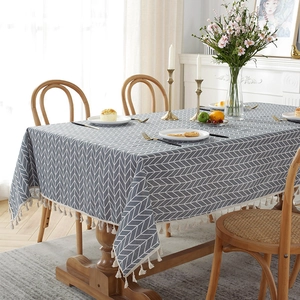 Detail of grey herringbone linen tablecloth featuring beige decorative fringe on wood table