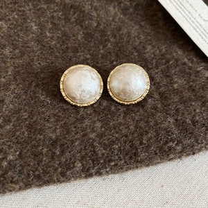 Detail of gold-plated geometric stud earrings with pearl centers on brown felt background