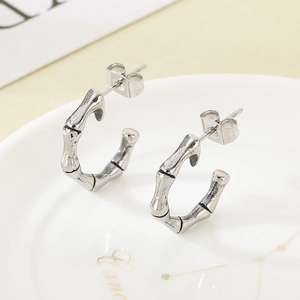 Detail of silver bamboo textured C-shaped hoop earrings on a white ceramic plate