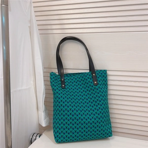 Close-up of green geometric print tote bag with black leather straps and gold rivets