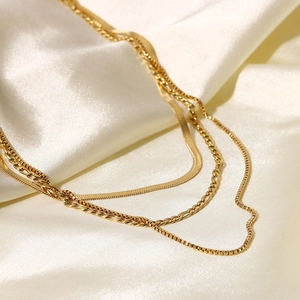 Three-layer gold snake chain and Figaro necklace set displayed on white silk fabric
