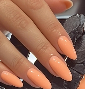 Faux ongles amande rose pêche brillant présentés sur un fond de roche noire texturée