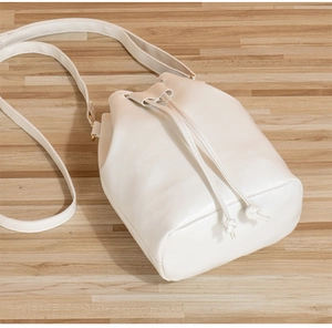 Detail of white faux leather bucket bag with drawstring closure on a wooden surface