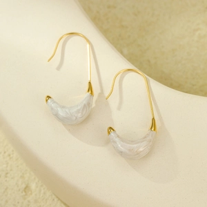 Macro detail of crescent C-shape gold earrings with marble inlay on stone surface