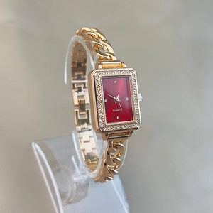 Detail of square gold watch with red dial and crystal bezel on a chain strap