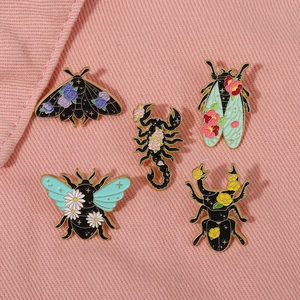 Detail of five enamel insect brooches with colorful floral patterns on a pink fabric background