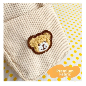 Detail of beige corduroy fabric with a cute plush bear embroidery on a small shoulder bag