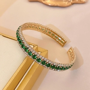 Macro detail of emerald-green and white zircon pavé setting on a gold open cuff bracelet