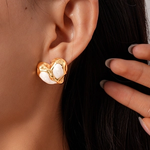 Close-up of gold and white enamel heart stud earring worn on model ear for scale