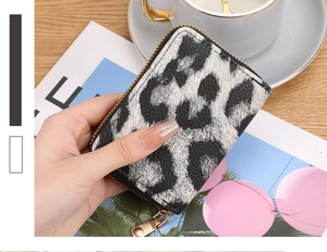 Close-up of a silver leopard print card holder with zipper held by a woman's hand