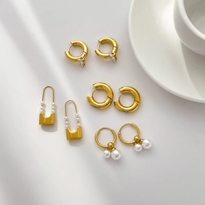 Elegant gold titanium steel earrings set with pearls and zircons on white minimalist background
