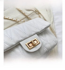 Close-up of white quilted crossbody bag with gold metal twist lock and chain strap detail