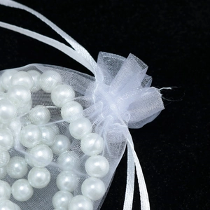 Macro shot of white organza drawstring gift bag with shiny pearls on black background
