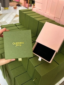 Detail of drawer jewelry boxes in green and pink with ribbon pull and gold logo