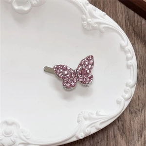 Close-up of a pink rhinestone butterfly hair clip on a white ceramic tray with wood background