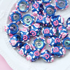 Macro shot of blue hand-painted glass beads with pink spirals on a white ceramic plate