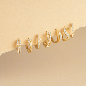 Close-up of assorted gold huggie hoop earrings with sparkling zircon stones on beige background